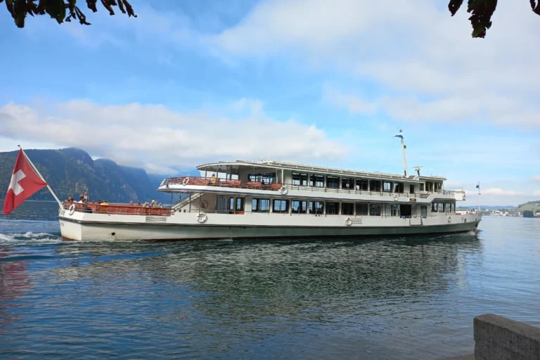 Scheduled Lake Lucerne boat trip under way with passengers on the open deck and a Swiss flag at the stern