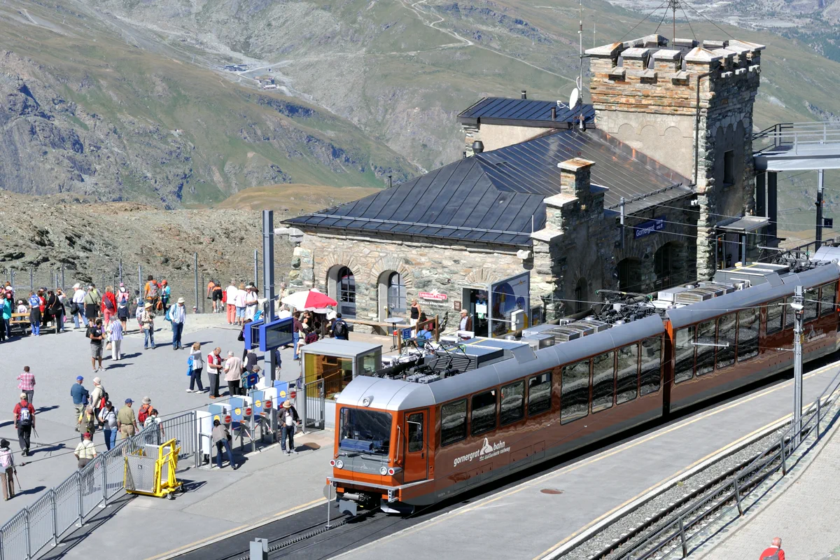 Gornergrat Bahn train at the summit station platform above Zermatt, passengers boarding under a clear blue sky