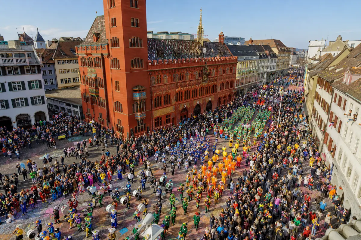 AI-generated elevated daytime view of a colorful Basel Carnival procession through the city.