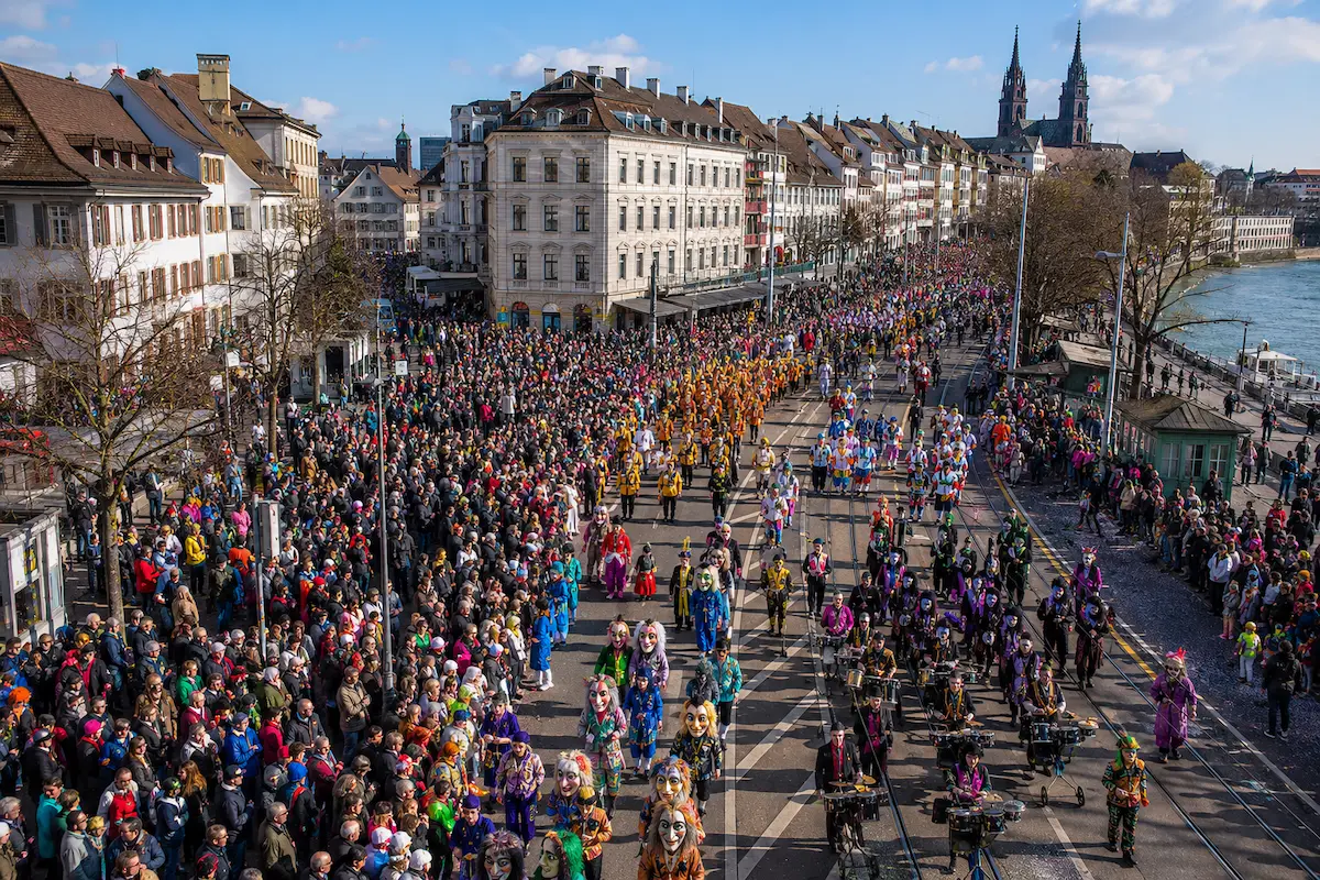 AI-generated elevated daytime view of a large Basel Carnival procession with the city in the background.