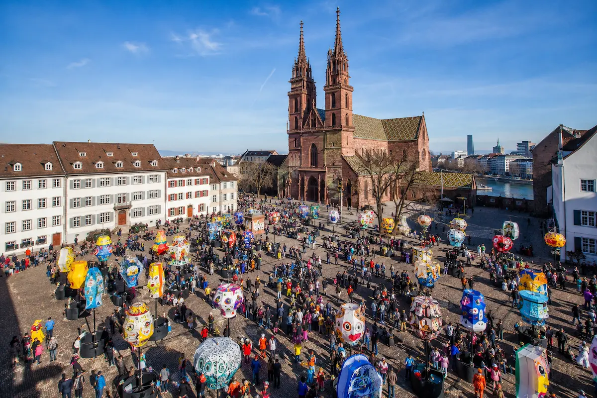 AI-generated elevated daytime illustration of colorful carnival lanterns in a Basel city square.