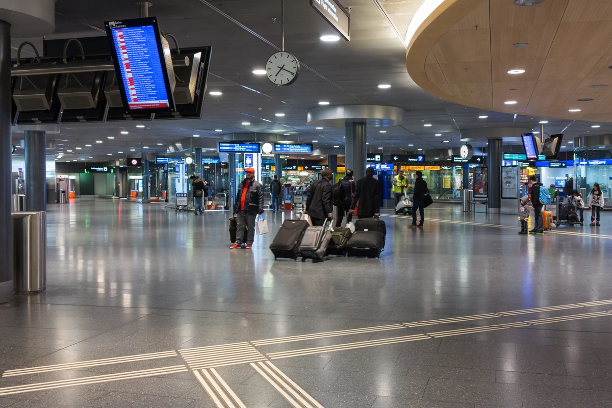 Travelers with luggage in the railway and shopping concourse at Zurich Airport