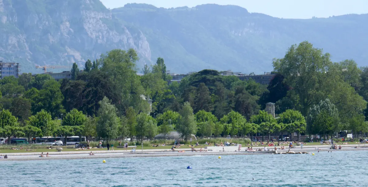 Eaux-Vives Beach on Lake Geneva with trees and mountains behind the shoreline