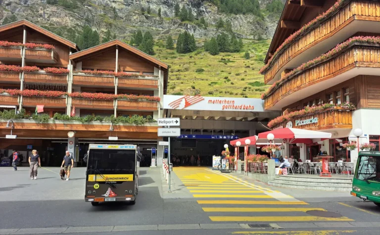Matterhorn Gotthard Bahn station entrance in Zermatt between chalet buildings and Alpine slopes
