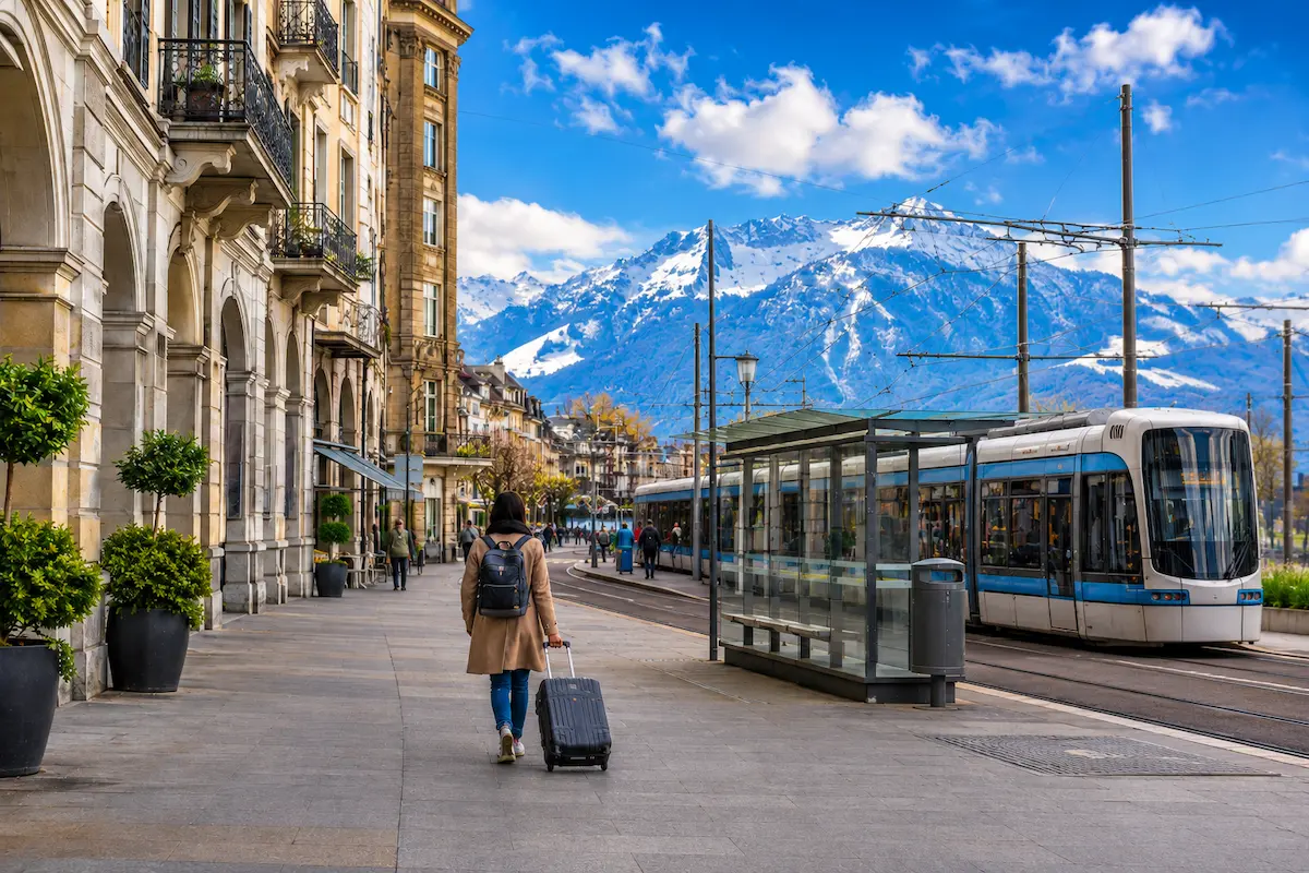 Wide travel scene of a traveler moving between Swiss cities with luggage