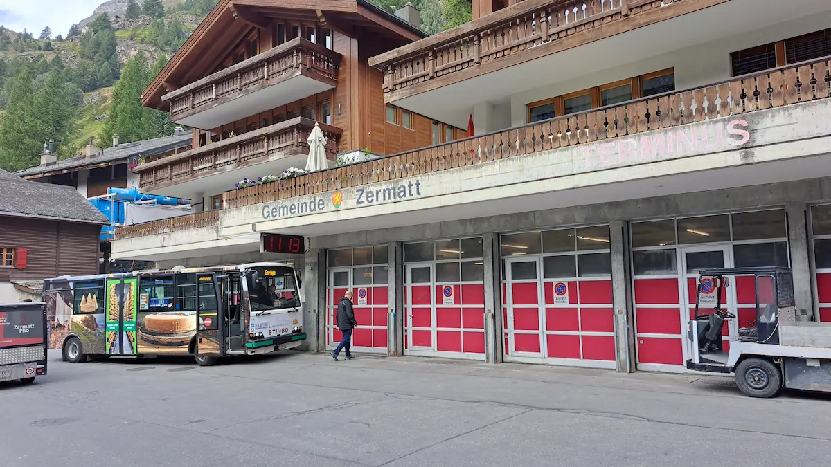 Electric local bus and service vehicle beside municipal buildings in Zermatt